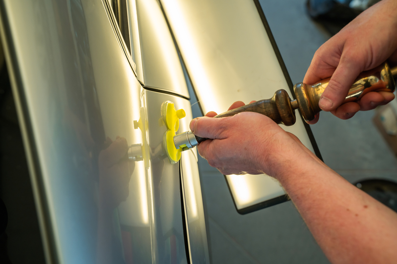 PDR technician using a dent puller on a car body panel.