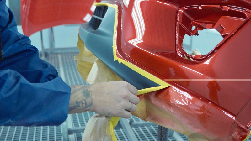 technician removing painters tape from recently painted bumper